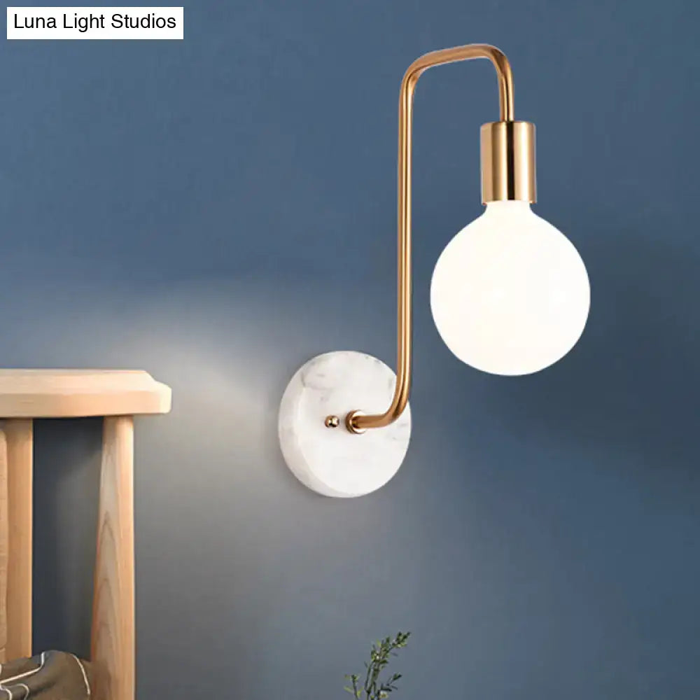 White glass sphere marble sconce with brass curved arm mounted on blue wall on Tampa Home & Garden Store