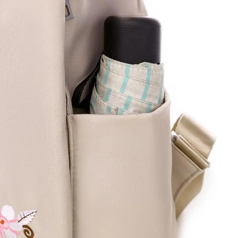 Beige waterproof backpack with side pocket holding a striped umbrella; anti-theft school bag on Tampa Home & Garden Store