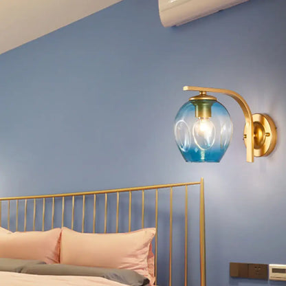 Decorbites modern gold curved arm glass wall sconce with blue glass shade beside bed on Tampa Home & Garden Store