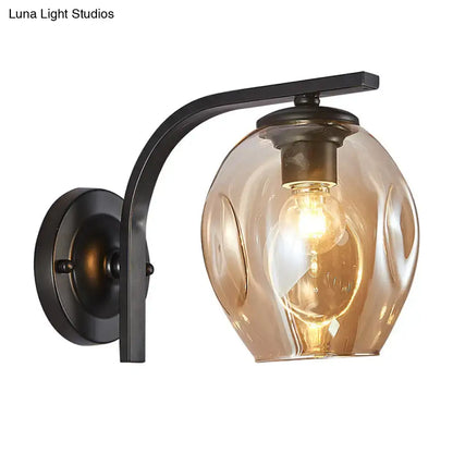 Modern curved-arm glass wall sconce with black metal mount and amber glass shade on Tampa Home & Garden Store