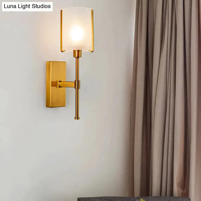 Gold frosted glass wall sconce with pencil arm and rectangular backplate, warm glow on Tampa Home & Garden Store