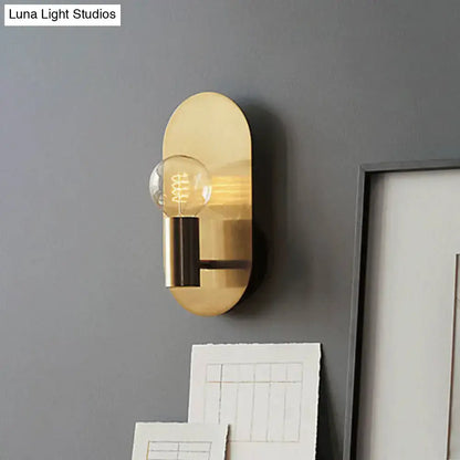 Gold metal bare-bulb sconce with exposed Edison bulb on oval backplate mounted to gray wall on Tampa Home & Garden Store