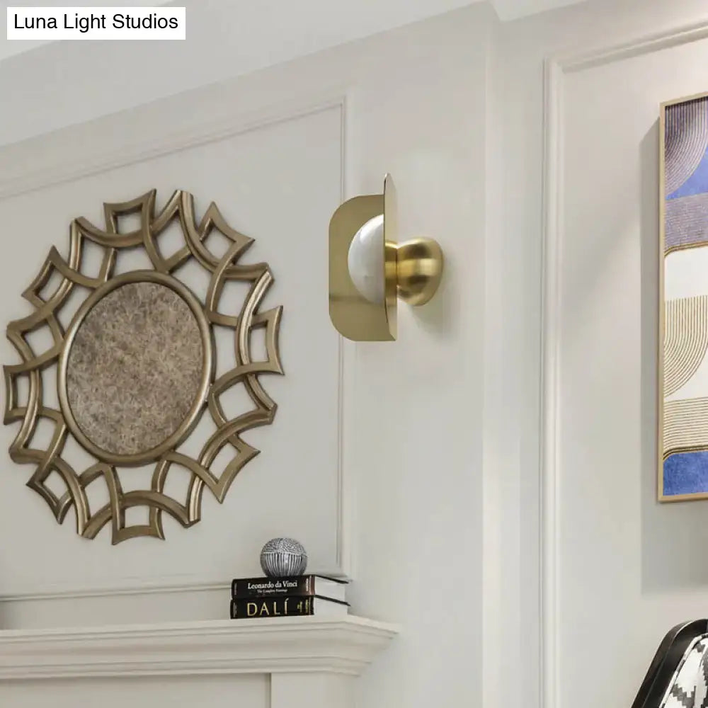 Gold curved metal wall sconce with white shade beside a sunburst mirror on white wall on Tampa Home & Garden Store