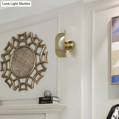 Gold curved metal wall sconce with white shade beside a sunburst mirror on white wall on Tampa Home & Garden Store