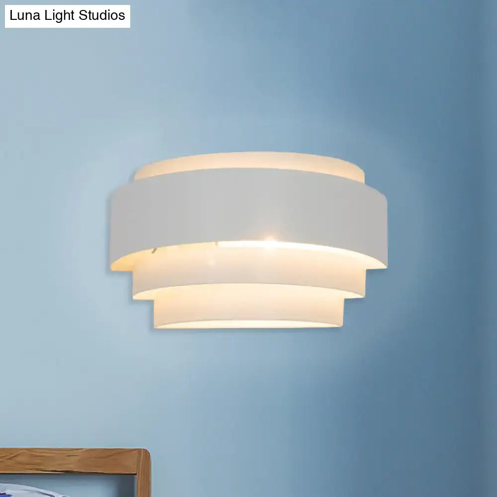 White tiered wall sconce with layered circular bands and warm glow on blue wall on Tampa Home & Garden Store