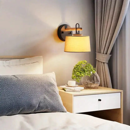 Modern grey drum shade wall lamp with wood arm above a nightstand in a cozy bedroom Decorbites on Tampa Home & Garden Store