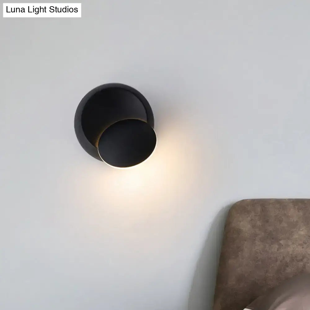Black circular wall light with overlapping disks casting a warm glow on a white wall on Tampa Home & Garden Store