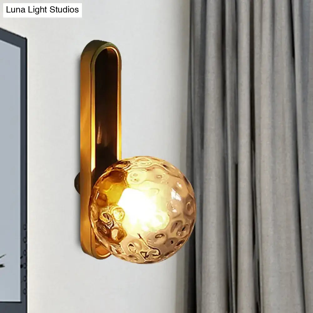 Gold wall sconce by Luna Light Studios with amber glass globe on wall beside gray curtains on Tampa Home & Garden Store