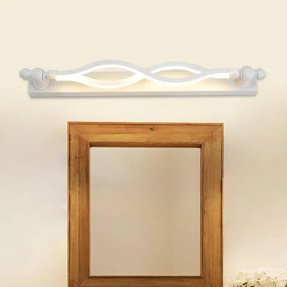Modern wavy white twist acrylic vanity sconce with warm glow above a wood-framed mirror on wall on Tampa Home & Garden Store