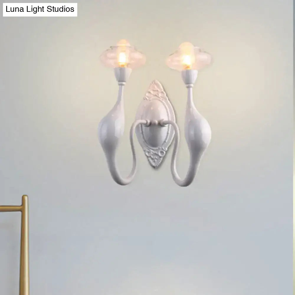 White ceramic dual-arm wall sconce with ornate backplate and glowing bulbs on Tampa Home & Garden Store