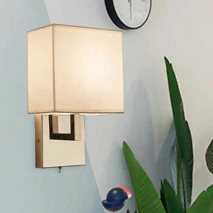 Beige gold wall sconce with square fabric shade and brass mount on a pale blue wall on Tampa Home & Garden Store