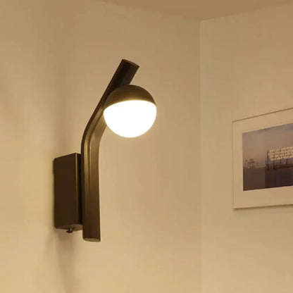 Black glass orb wall sconce with curved matte black metal arm, illuminated on Tampa Home & Garden Store