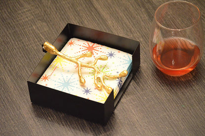 Vibhsa napkin holder with gold olive bud design on black tray beside a colorful patterned napkin on Tampa Home & Garden Store