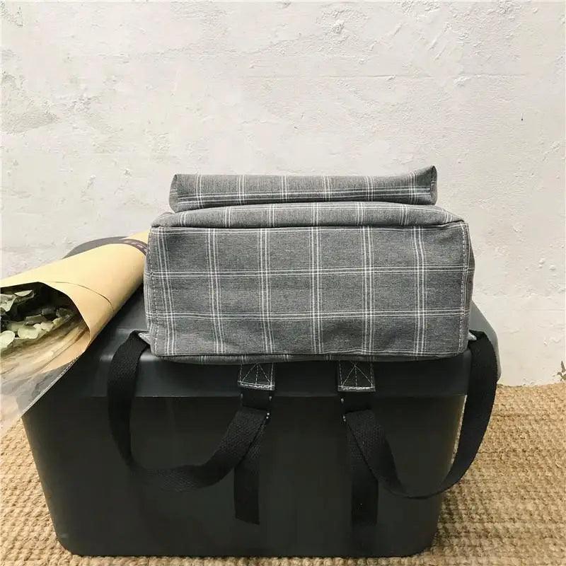 Stevvex gray plaid school backpack with black straps resting on a black storage box on Tampa Home & Garden Store