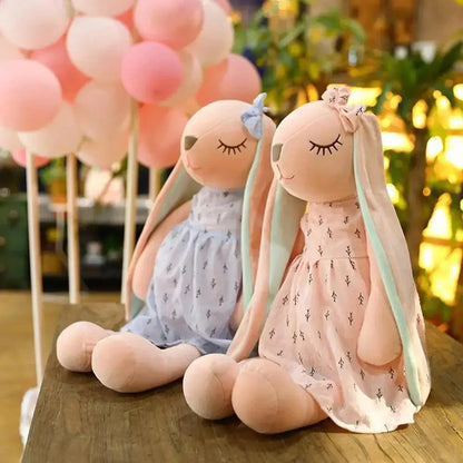 Stevvex plush bunny dolls in pastel dresses with long ears and bows, on wood table with pink balloons on Tampa Home & Garden Store