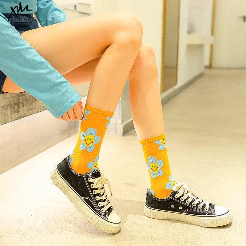 Stevvex crew socks orange pair with blue flower patches and smiley faces worn with black sneakers on Tampa Home & Garden Store