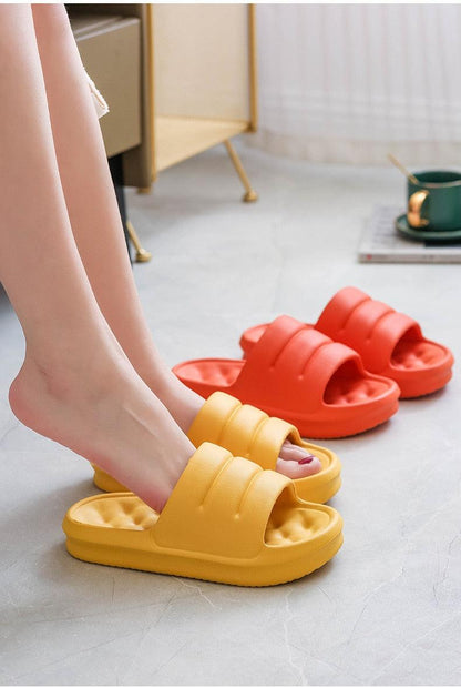 Thick EVA sofa slides sandals in yellow worn by feet with an orange pair in the background on Tampa Home & Garden Store