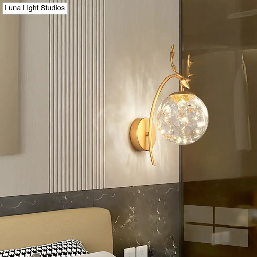 Black Antler Wall Sconce with gold antler arm and glass globe lit by warm string lights on Tampa Home & Garden Store