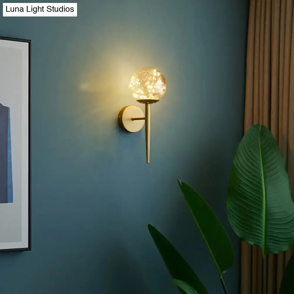 Gold Glass Globe Wall Sconce with brass mount emits warm glow on teal wall on Tampa Home & Garden Store