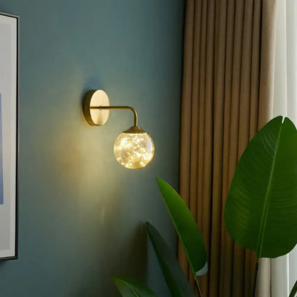 Decorbites Gold Glass Globe Wall Sconce with brass arm and warm string lights on teal wall on Tampa Home & Garden Store