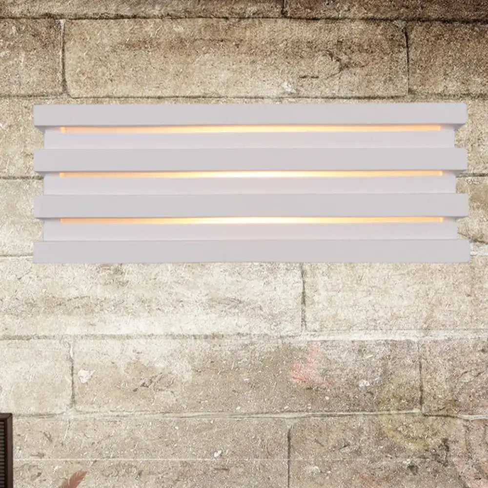 White louvered wall sconce by Decorbites with slatted design and warm glow on stone wall on Tampa Home & Garden Store
