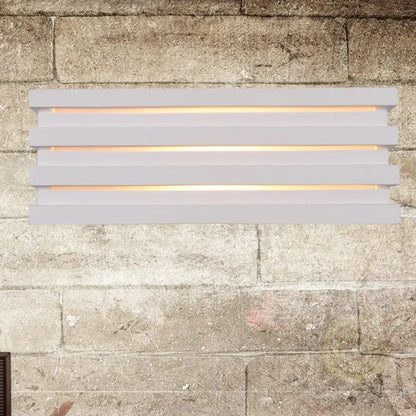 White louvered wall sconce by Decorbites with slatted design and warm glow on stone wall on Tampa Home & Garden Store