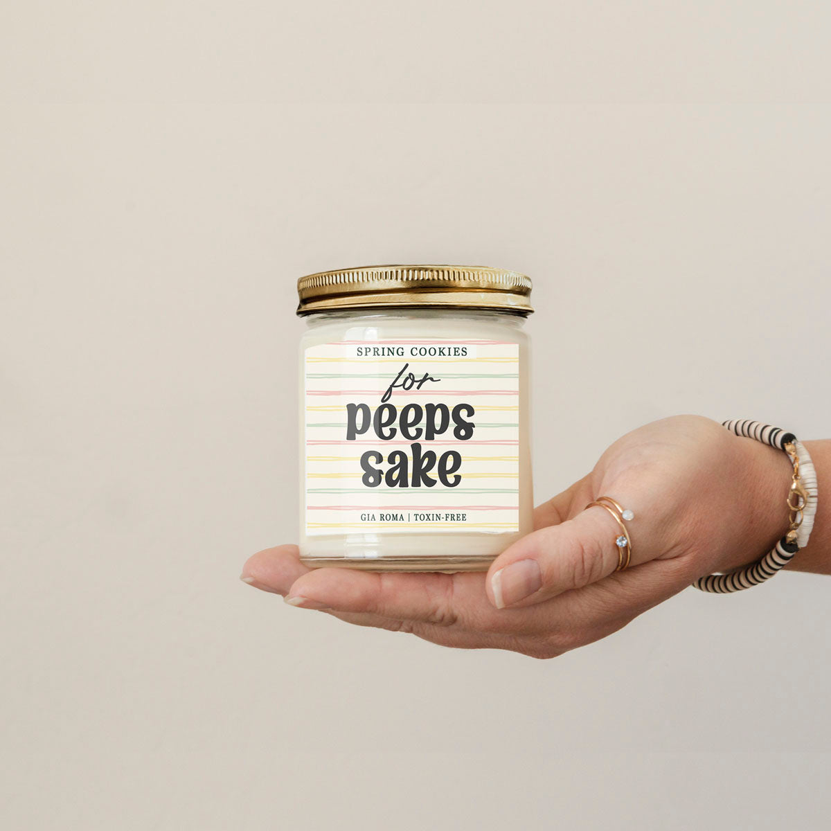 Easter Cookie Candle by Gia Roma held in hand; white glass jar with pastel striped label and gold lid on Tampa Home & Garden Store