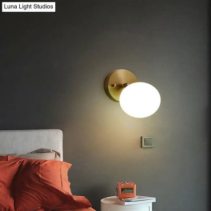 Brass glass wall sconce with a round white globe mounted on gray wall above a nightstand on Tampa Home & Garden Store