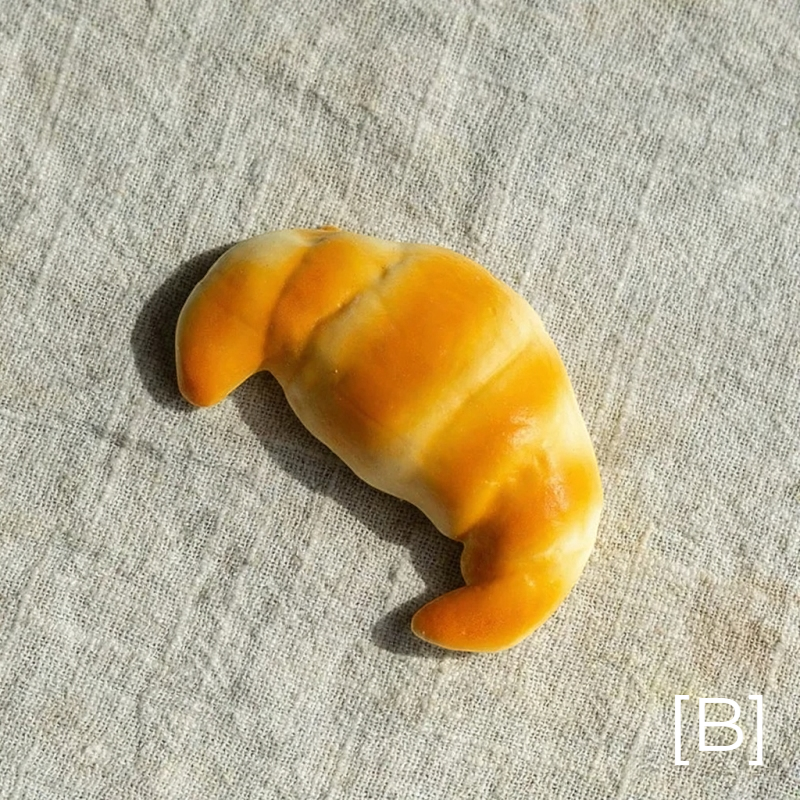 Artificial croissant pastry prop RusticReach in orange-yellow tones on fabric backdrop on Tampa Home & Garden Store
