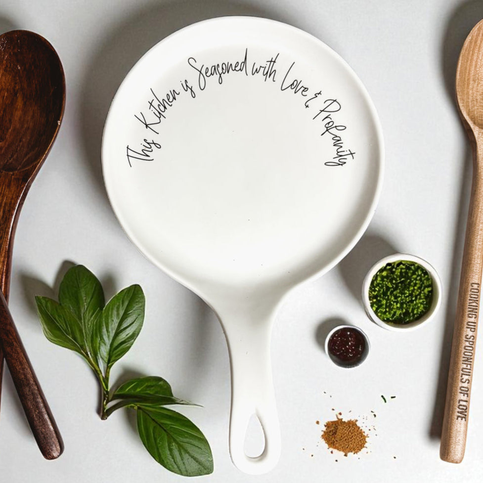 Love & Profanity spoon rest, white round kitchen accessory with rim text, two spoons nearby on Tampa Home & Garden Store