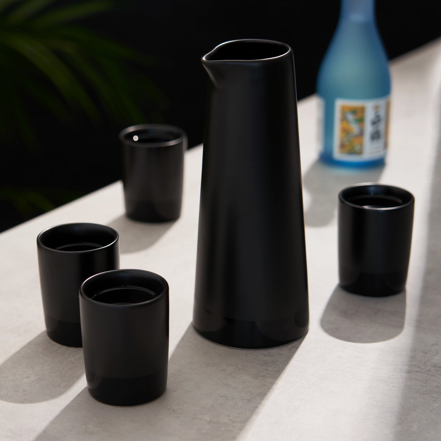 Four Black Stoneware Sake Tumblers and Carafe