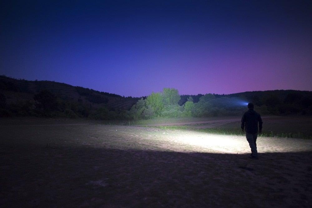 Stevvex rechargeable flashlight casts bright beam across night field with hiker silhouette on Tampa Home & Garden Store