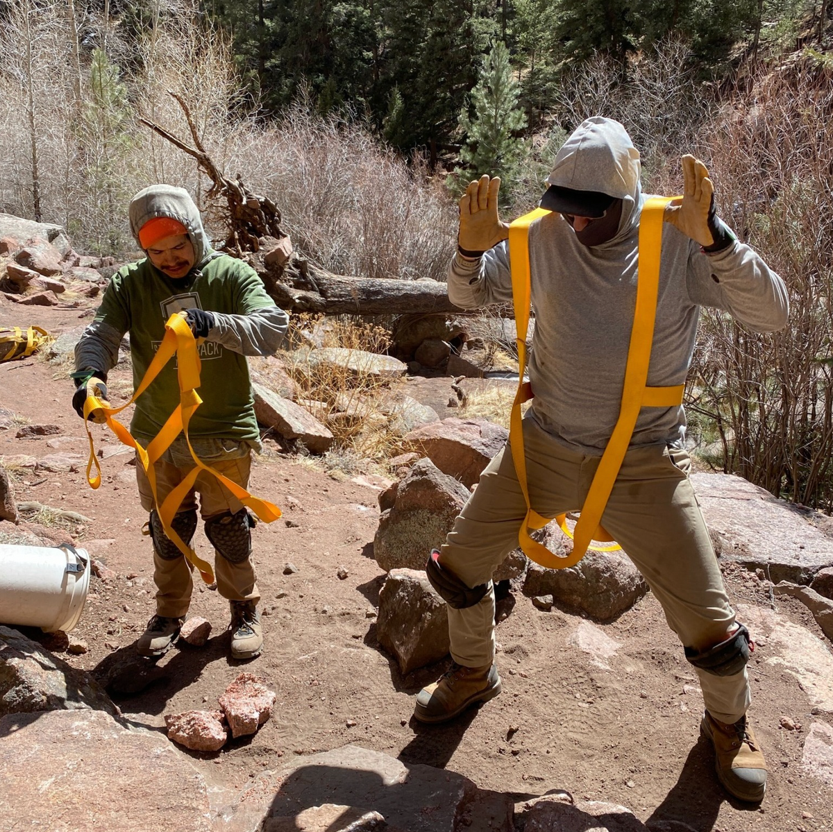 Rock Belt safety harness by Backslope Tools, yellow straps on rocky terrain with two workers on Tampa Home & Garden Store
