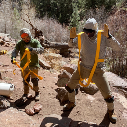 Rock Belt safety harness by Backslope Tools, yellow straps on rocky terrain with two workers on Tampa Home & Garden Store