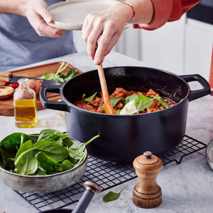 Enameled cast iron round Dutch oven 5-Qt, black exterior being stirred with a wooden spoon on Tampa Home & Garden Store