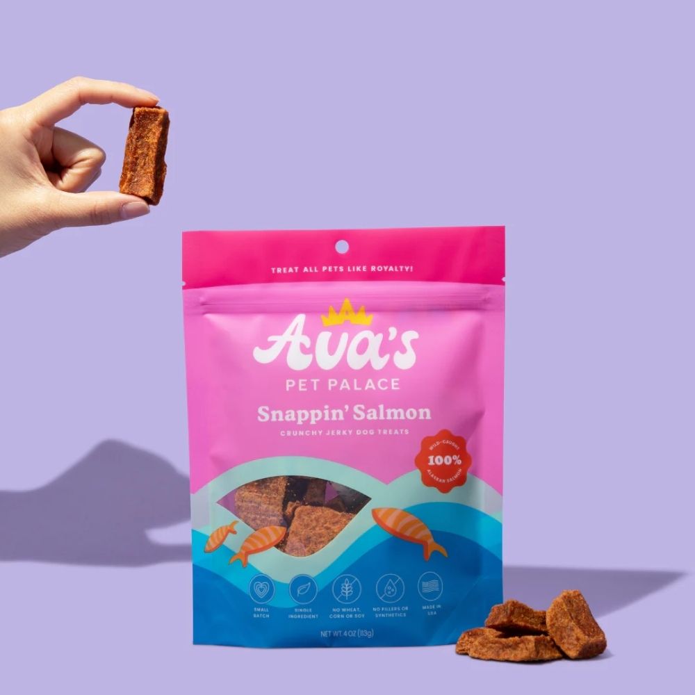 Ava's Pet Palace Snappin' Salmon crunchy jerky dog treats 4 oz in pink bag hand holds brown piece on Tampa Home & Garden Store