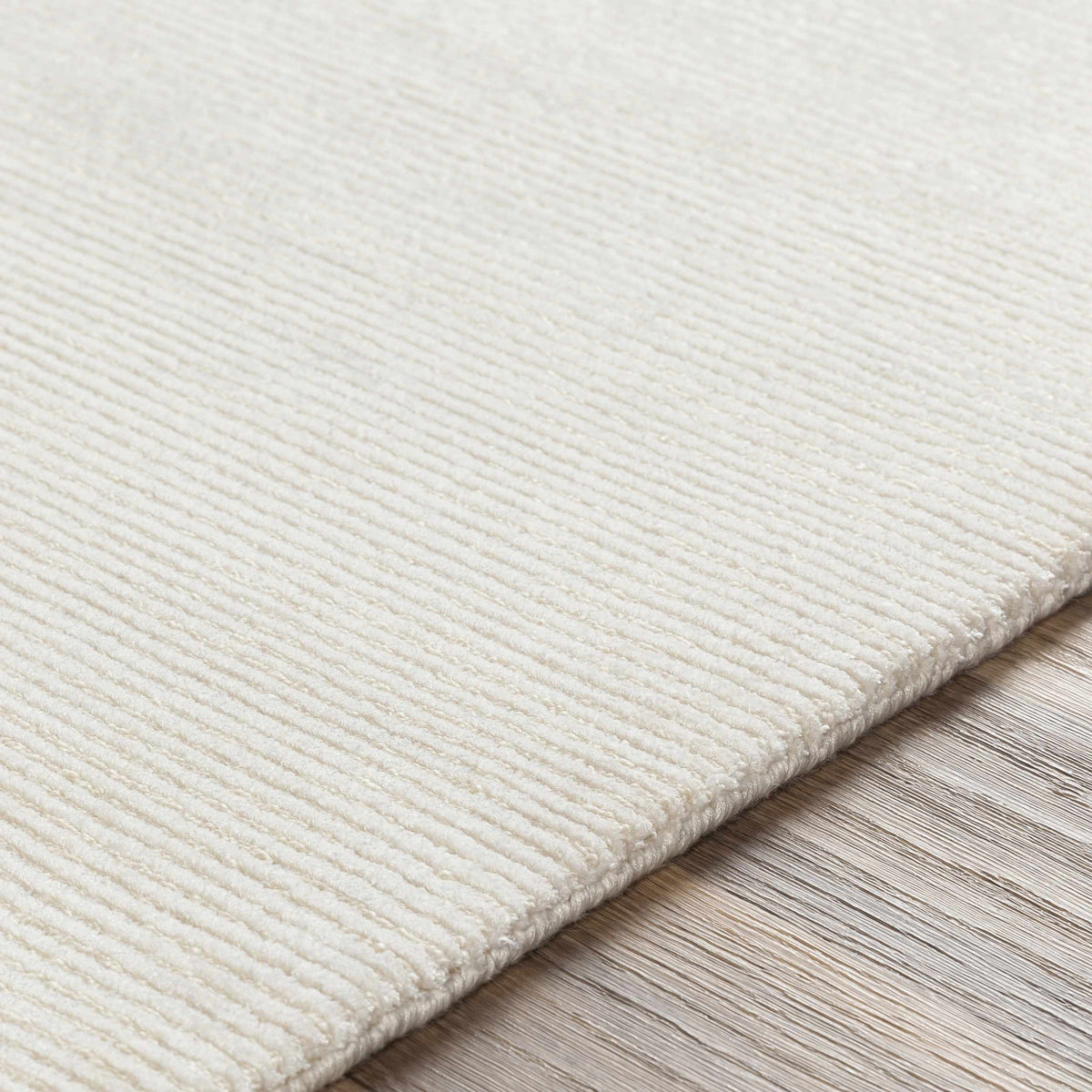 Sabinsville Carpet rug in ivory, textured pile, rolled and stacked on a wood floor on Tampa Home & Garden Store