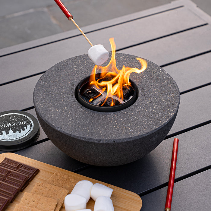 Concrete semi-round fire pit outdoors with glowing flame, dark gray finish by City Bonfires on Tampa Home & Garden Store