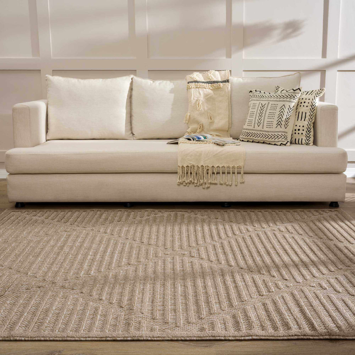 Anah Tan Outdoor Rug by Boutique Rugs; tan woven with fringe, in front of a beige sofa on Tampa Home & Garden Store