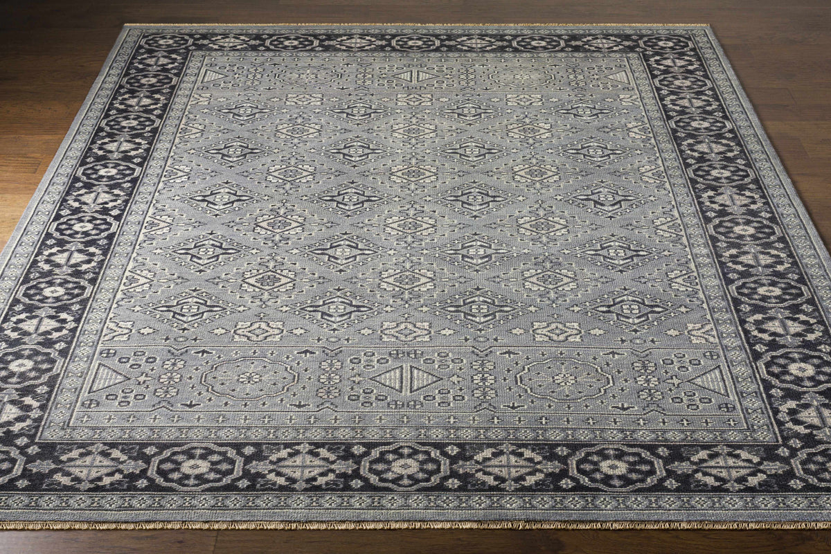 Sherwood Area Rug, gray field with diamond motifs and dark navy border with fringe on wood floor on Tampa Home & Garden Store