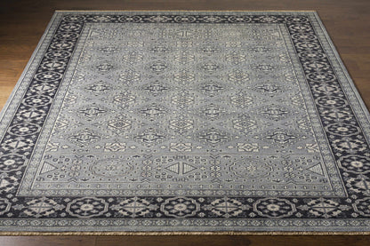 Sherwood Area Rug, gray field with diamond motifs and dark navy border with fringe on wood floor on Tampa Home & Garden Store