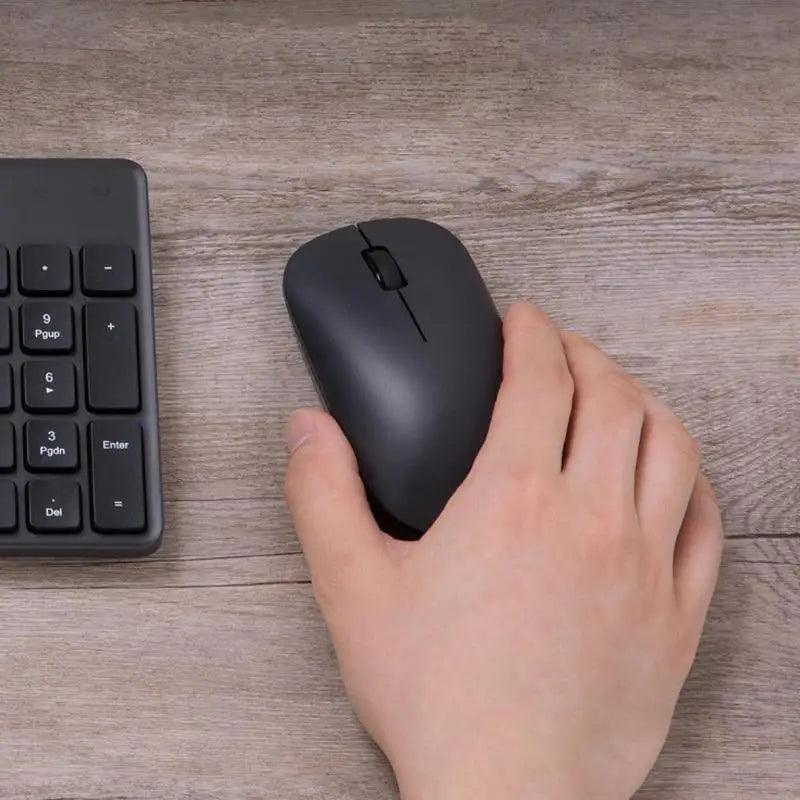 Black wireless optical mouse with USB/Bluetooth, held in hand beside a keyboard on wood desk on Tampa Home & Garden Store