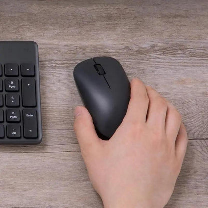 Black wireless optical mouse with USB/Bluetooth, held in hand beside a keyboard on wood desk on Tampa Home & Garden Store