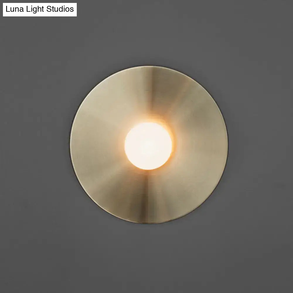 Brushed brass wall sconce with circular backplate and glowing bulb Luna Light Studios watermark on Tampa Home & Garden Store
