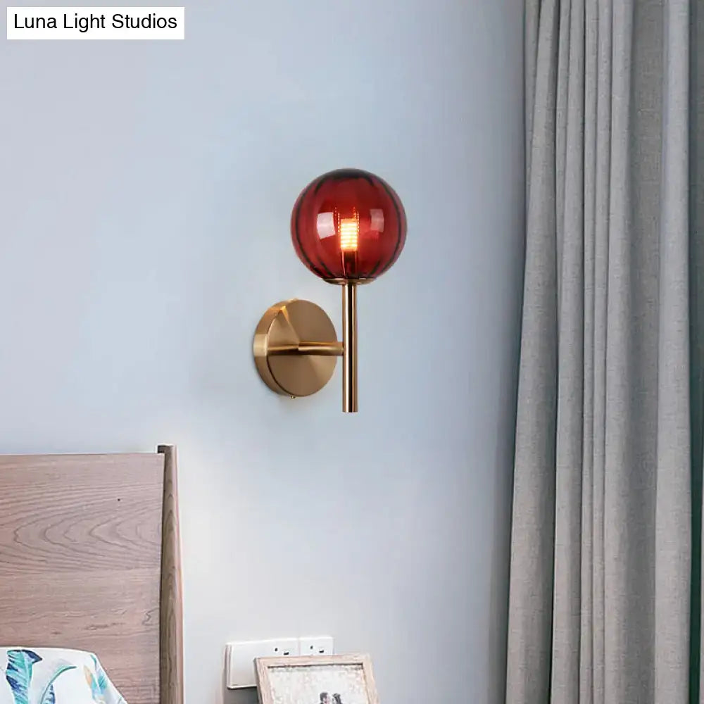 Amber red glass wall sconce with brass mount on pale blue wall beside a bed on Tampa Home & Garden Store