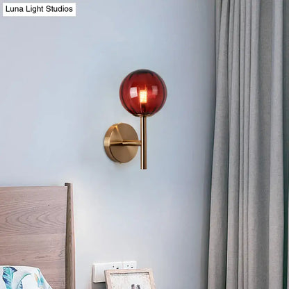 Amber red glass wall sconce with brass mount on pale blue wall beside a bed on Tampa Home & Garden Store