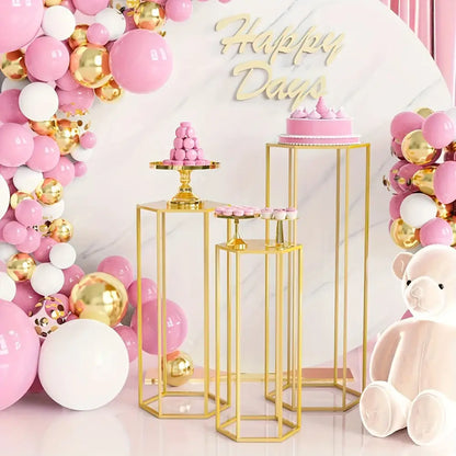 Gold hexagonal vase set on tall gold stands amid pink and gold balloon backdrop with cake on Tampa Home & Garden Store