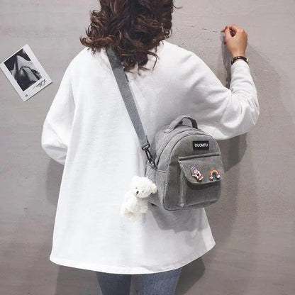 Stevvex small gray backpack with front pocket patches and a white teddy keychain worn crossbody on Tampa Home & Garden Store