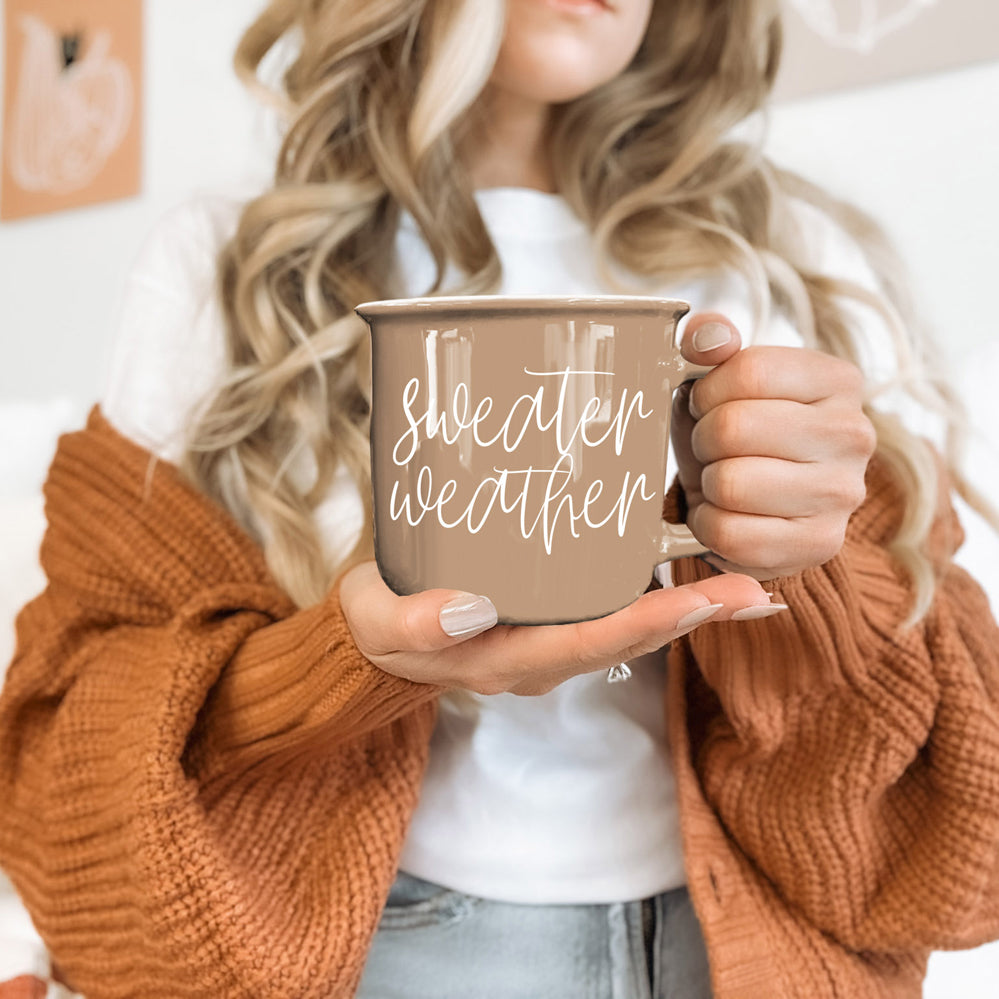 Coffee mug Gia Roma Sweater Weather taupe with white script held by hands wearing rust cardigan on Tampa Home & Garden Store