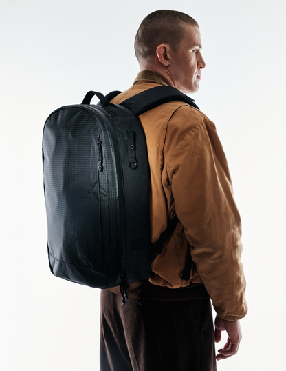 Conceal Pack 21L backpack by The Brown Buffalo black gridtext fabric worn with brown jacket on Tampa Home & Garden Store